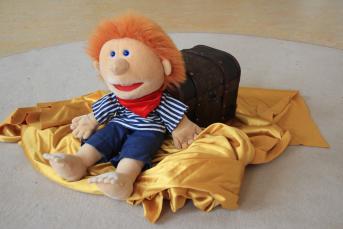 Handpuppe Feuerhaar lehnt an einer Truhe (Steht für das Schulspiel) 